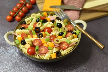 Durum wheat semolina pasta salad made with peppered salami cherry vine tomatoes red leicester cheese spring onions black and green pitted olives.