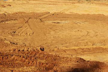 Arid open-pit mine landscape with intricate dirt tracks and various soil mounds under harsh...
