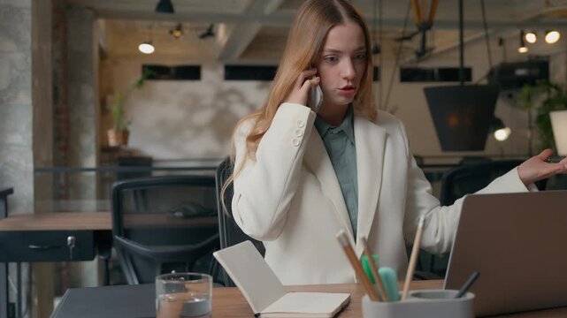 Annoyed confused stressed multitasking business Caucasian woman businesswoman writing notes typing laptop talking mobile phone troubled bad news overworked employer girl female in office arguing talk - Powered by Adobe