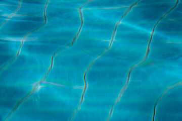 Abstract close-up of sunlight reflections creating wavy patterns on clear blue water surface
