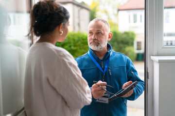 Man in blue jacket speaks with woman at doorway during daytime in residential neighborhood