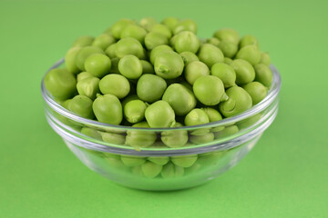 Young green peas in a bowl on a green background. Close-up.	