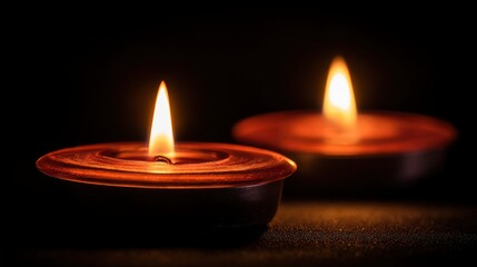Two small candles in metal holders burn against a dark background their light illuminating a textured surface