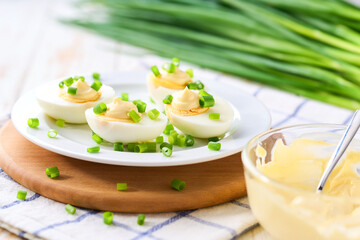 Boiled chicken eggs and glass bowl with a mayonnaise and cut chives on a light kitchen table.