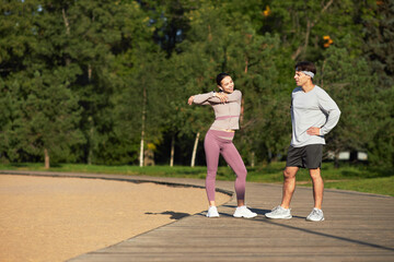 Young Asian woman stretching arms while standing on wooden path outdoors next to middle aged...