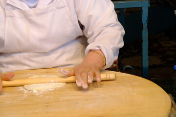 Close-up of a woman's hand rolling out flatbread dough with a rolling pin. Traditional Turkish pastries. Flatbread dough. A woman's hand rolling out dough with a rolling pin on a wooden table.