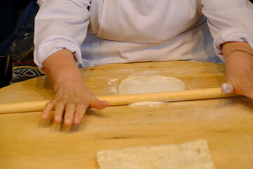 Close-up of a woman's hand rolling out flatbread dough with a rolling pin. Traditional Turkish pastries. Flatbread dough. A woman's hand rolling out dough with a rolling pin on a wooden table.