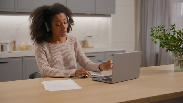 African American woman at home writing notes looking laptop listening music in headphones audio sound enjoying song singing noting e-learning girl female student with computer at kitchen happy study