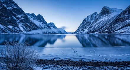 Majestic snow capped mountains reflected in a calm icy lake under a clear blue sky