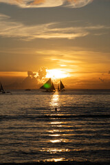 Sailboats gliding on calm sea during golden sunset with vibrant orange sky and reflections on water