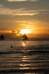 Sailboats gliding on calm sea during golden sunset with vibrant orange sky and reflections on water
