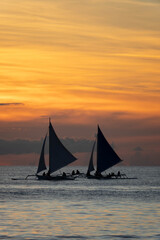 Silhouetted sailboat gliding on calm sea at sunset with vivid orange and golden sky