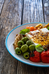 Greek style appetizer - feta cheese with olives and grilled tomatoes, garlic and shallot on wooden table	