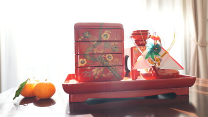 明るい窓辺に置かれた、正月の屠蘇器とおせち料理の重箱と葉付きのミカン　(4459)
