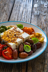 Greek style appetizer - feta cheese with olives and grilled tomatoes, garlic and shallot on wooden table	