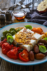 Greek style appetizer - feta cheese with olives and grilled tomatoes, garlic and shallot on wooden table	