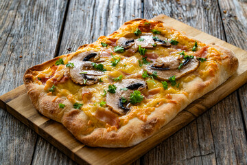 Mini pinsa with cheddar cheese, boiled ham and white mushrooms on wooden table
