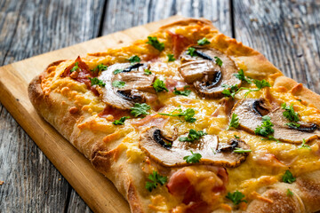 Mini pinsa with cheddar cheese, boiled ham and white mushrooms on wooden table