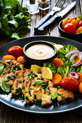 Grilled chicken breast, mayonnaise and vegetables on wooden table	
