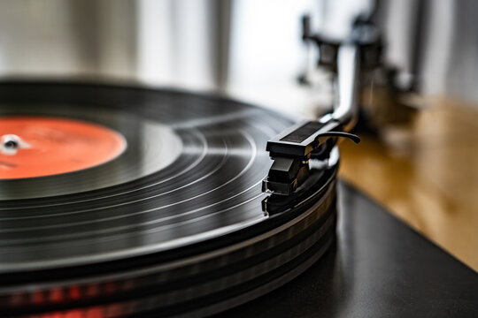 Close-up of spinning vinyl record on turntable, capturing motion of grooves and stylus. Classic analog music setup evokes nostalgia, creativity and warm sound