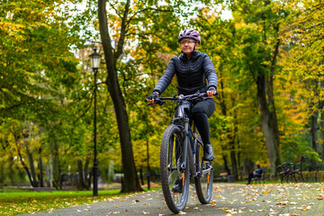 Naklejka premium Middle aged beautiful woman riding bicycle in city park in autumn. Front view 