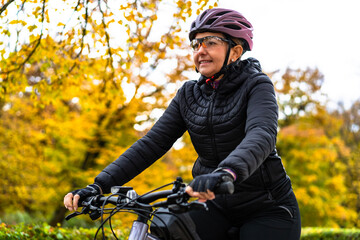 Middle aged beautiful woman riding bicycle in city park in autumn. Side view