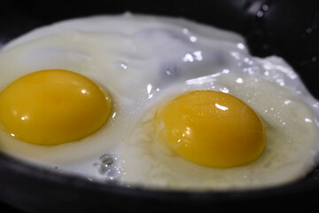 Cooking two sunny-side-up eggs in a frying pan on a stovetop during breakfast preparation