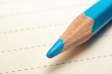 The point of a blue pencil touching a piece of paper with a dotted line, close-up macro shot