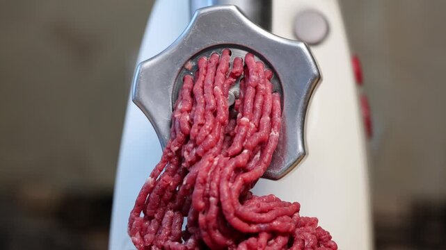 Close-up front video shot of process of meat grinding in the kitchen with electric mincing machine on blurred background