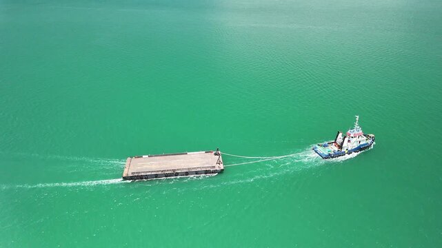 a tugboat towing a large flat barge across calm turquoise water showcasing maritime strength teamwork and the beauty of industrial activity on a bright clear day