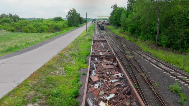 Long line of scrap wagons stretches along rails beside green country road