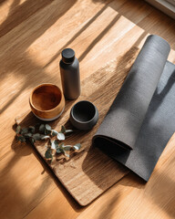 Wellness essentials including yoga mat, diffuser, and wooden bowls arranged on wooden surface, creating serene atmosphere
