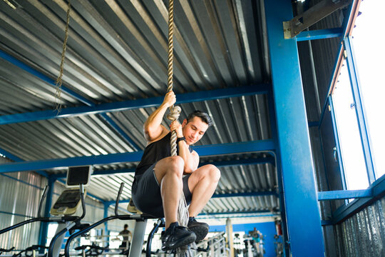Athletic man climbing rope in gym for fitness workout