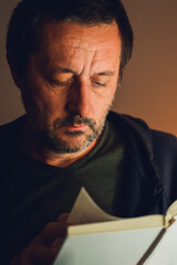 Low key portrait of mature man immersed in a book under warm light, capturing solitude, focus, and quiet intellectual contemplation.