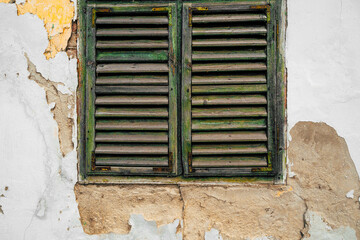 Old wooden window with venetian shutters on a ruined cracked wall, symbol of decay and passage of time.