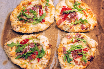 Freshly baked homemade Greek peinirli pastries topped with mozzarella cheese, bacon, paprika, and arugula, sprinkled with sesame seeds and oregano.