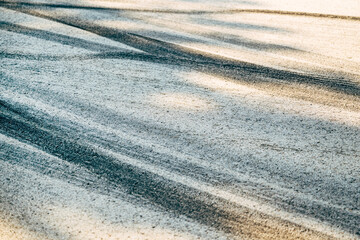Closeup of black tread skid marks on asphalt road surface, showing vehicle tire traces and textured pavement detail.
