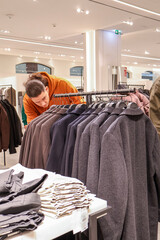 Modern man choosing clothes in a fashion store, trying on a coat, shopping for winter outfits in contemporary retail space. Lifestyle and consumer behavior concept.