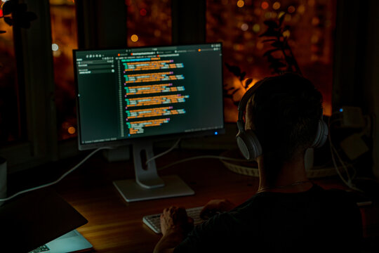 A young male programmer in front of a window with a lights of night city, on his laptop screen is code. out of focus - Powered by Adobe