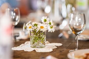 Glass of white wine and daisies on rustic table.