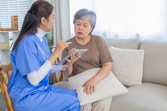 Asian senior elderly woman consulting with caregiver nurse female, discuss healthcare plan using digital tablet, focusing on medical advice, treatment progress, and patient wellness, at nursing home