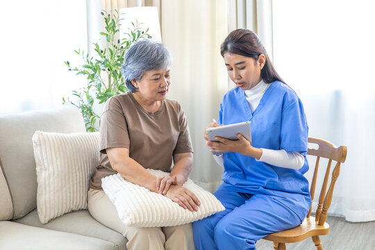 Asian senior elderly woman consulting with caregiver nurse female, discuss healthcare plan using digital tablet, focusing on medical advice, treatment progress, and patient wellness, at nursing home