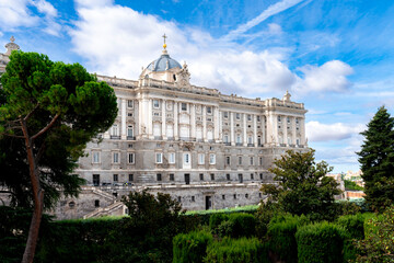 Obraz premium Close exterior view of the Royal Palace of Madrid Spain, highlighting its baroque and neoclassical design, surrounded by gardens and trees, with daylight sky and historic details reflecting heritage