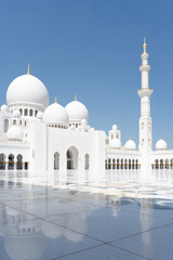 Vertical shot of beautiful white marble mosque with shiny square in foreground, United Arab Emirates