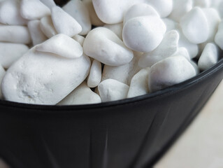 close-up of clean white smooth decorative pebbles or stones overflowing a black flower pot, texture...