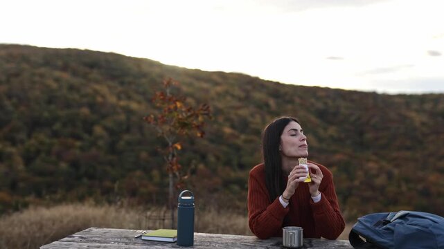 Young woman happily eating a cereal bar in an outdoor nature setting during autumn, promoting a healthy lifestyle and energy. 4k video