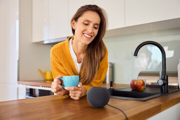 Smiling woman in kitchen talking to smart speaker