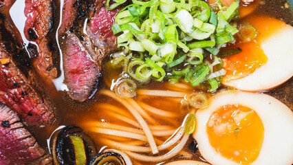 Succulent rare beef ramen in a beautiful bowl with bamboo shoots, spring onions, tamago (Japanese marinated egg), and leeks. Rich broth, authentic Japanese flavors.