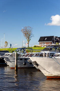 Modern luxury boats moored at Zwartsluis Netherlands canal marina bright sunlight modern houses trees background. Calm water reflects the vessels and blue sky, creating a serene Dutch coastal scene