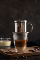 Traditional method of making Vietnamese coffee with condensed milk on black background. Close up. Vertical format.